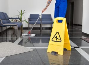 A wet floor sign in front of a worker mopping a floor. 