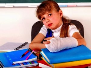 a little girl sat at a desk with schoolbooks. Her arm is in a cast.