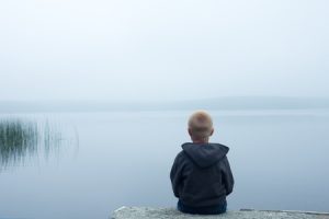 A young boy sitting alone beside a lake