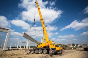 A large yellow crane lifting a large concrete rod.