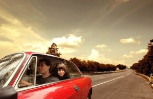 A car on the road with an adult sitting in the front and a child sat in the rear