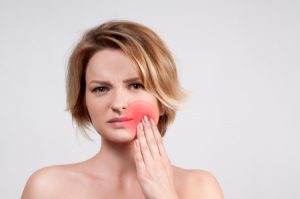 A woman presses broken jaw that is radiating red pain. 