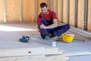 A man on the floor holding his leg after a workplace injury. He may be questioning 'will Suing My Employer Create Problems?'