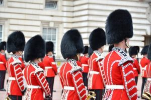 British Army soldiers in scarlet ceremonial uniforms and bearskin hats stand at attention
