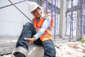 A construction worker holds their leg in pain