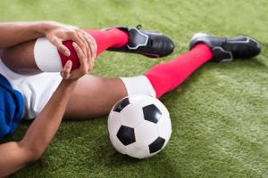 A footballer lying on the field holding his knee in pain.