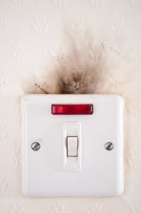 A wall switch with black residue from an electrical burn above it.