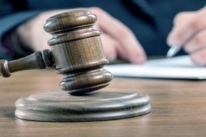 A close up shot of a gavel in front of a solicitor who is sat at a desk and filling out a form