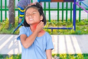A child holding her neck in pain. The painful area is highlighted in red.