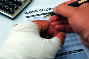 Someone with a bandage around their left hand writing in a work injury form. 