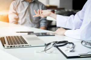 A doctor discussing breast cancer misdiagnosis stories with a patient while sat at a desk