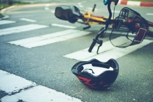 A bike on its side in the middle of a zebra crossing with an upside helmet next to the bike.
