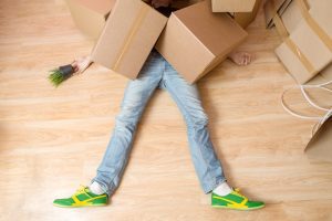 A man laying on the ground under a pile of cardboard boxes since he has been hit by heavy boxes at work