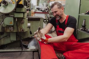 A factory worker in red overalls holding his wrist in pain