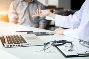 Doctors in discussion at a desk with a laptop, a clipboard and a stethoscope about Compensation For Wrongly Prescribed Antidepressants