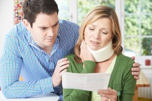 A husband and wife reading a letter about the wife's accident at work claims process as she clutches at her neck collar.