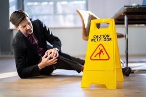 A man holding his knee in pain next to a wet floor sign due to slipping on a wet floor.