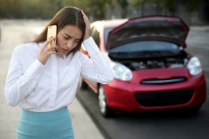 A woman on the phone next to her car with the bonnet open.