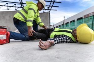 A construction employee lies on the ground while their colleague tries to help them after an accident happened.