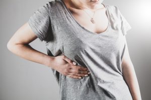 A woman holding the side of her ribs in pain.