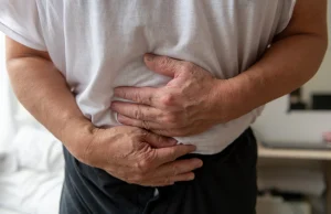 A man in a white shirt holds their stomach with both hands