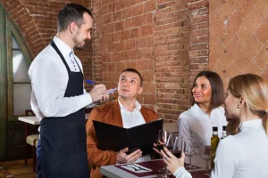 A server in a black apron takes order from 3 seated customers