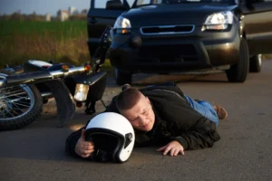 A man lying on the road with spinal injuries next to a motorbike with a car in the background 